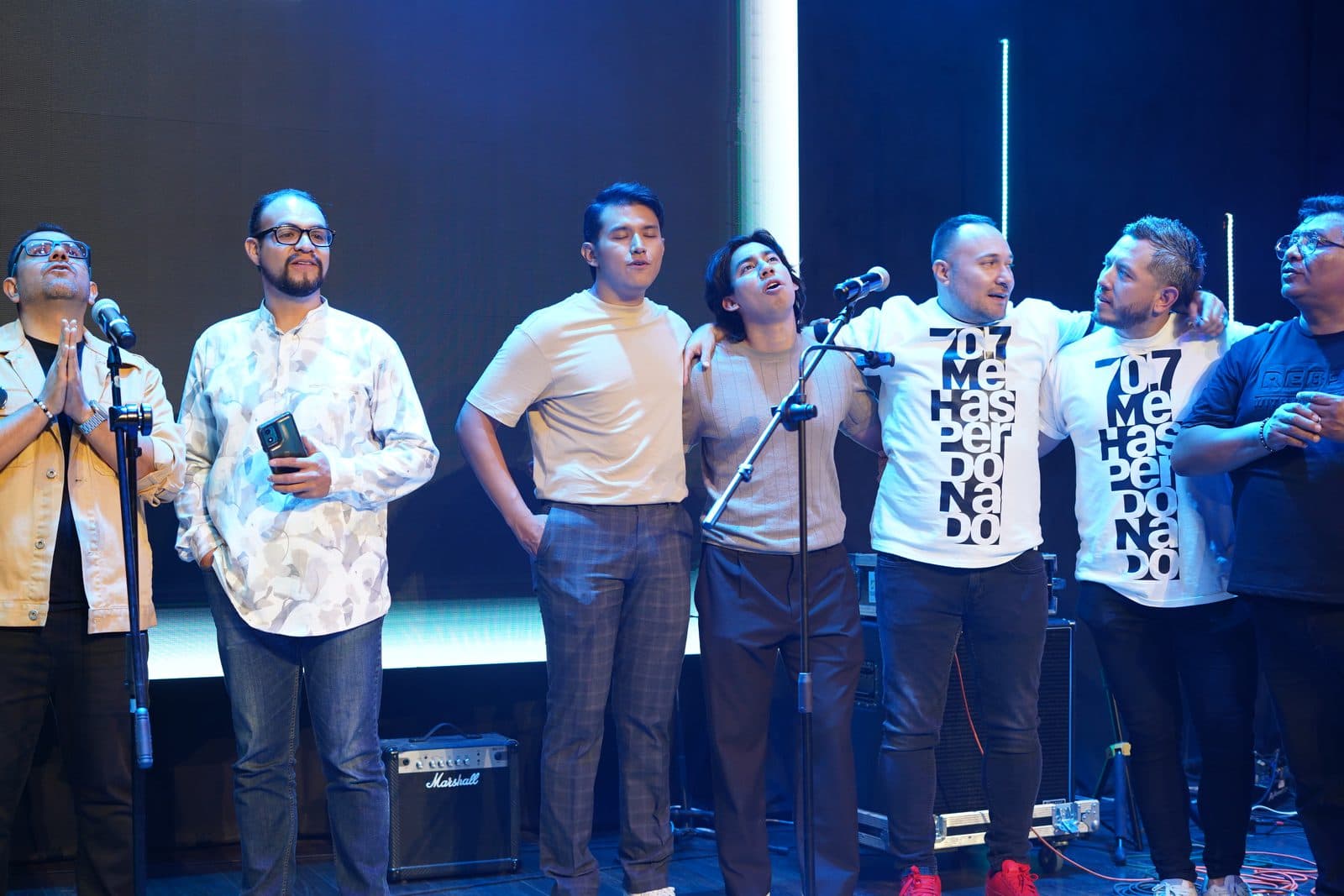 Músicos de distintas bandas abrazados por los hombros, cantando juntos