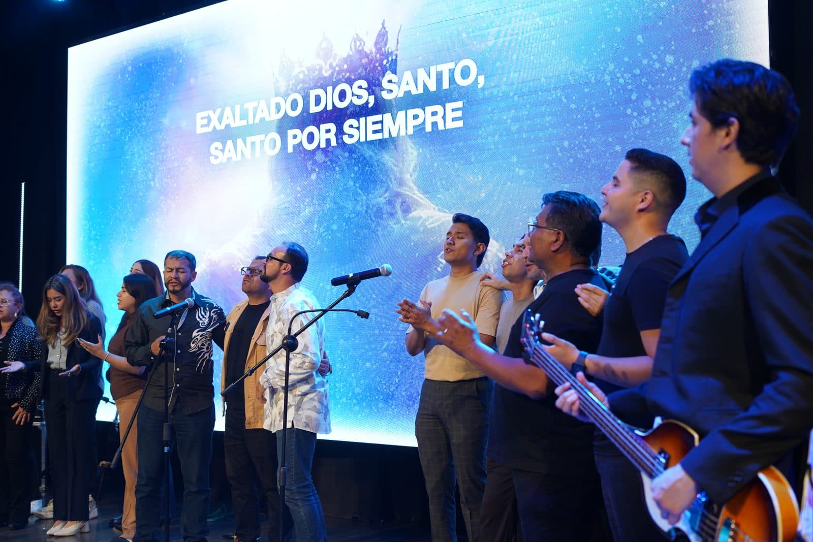 Artistas cantando juntos frente a una pantalla luminosa con la letra «Exaltado Dios, Santo, Santo por siempre»